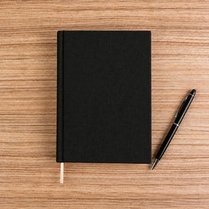 Blank black canvas notebook with pen on a wood desk – plain unprinted cover | Pamusan.com