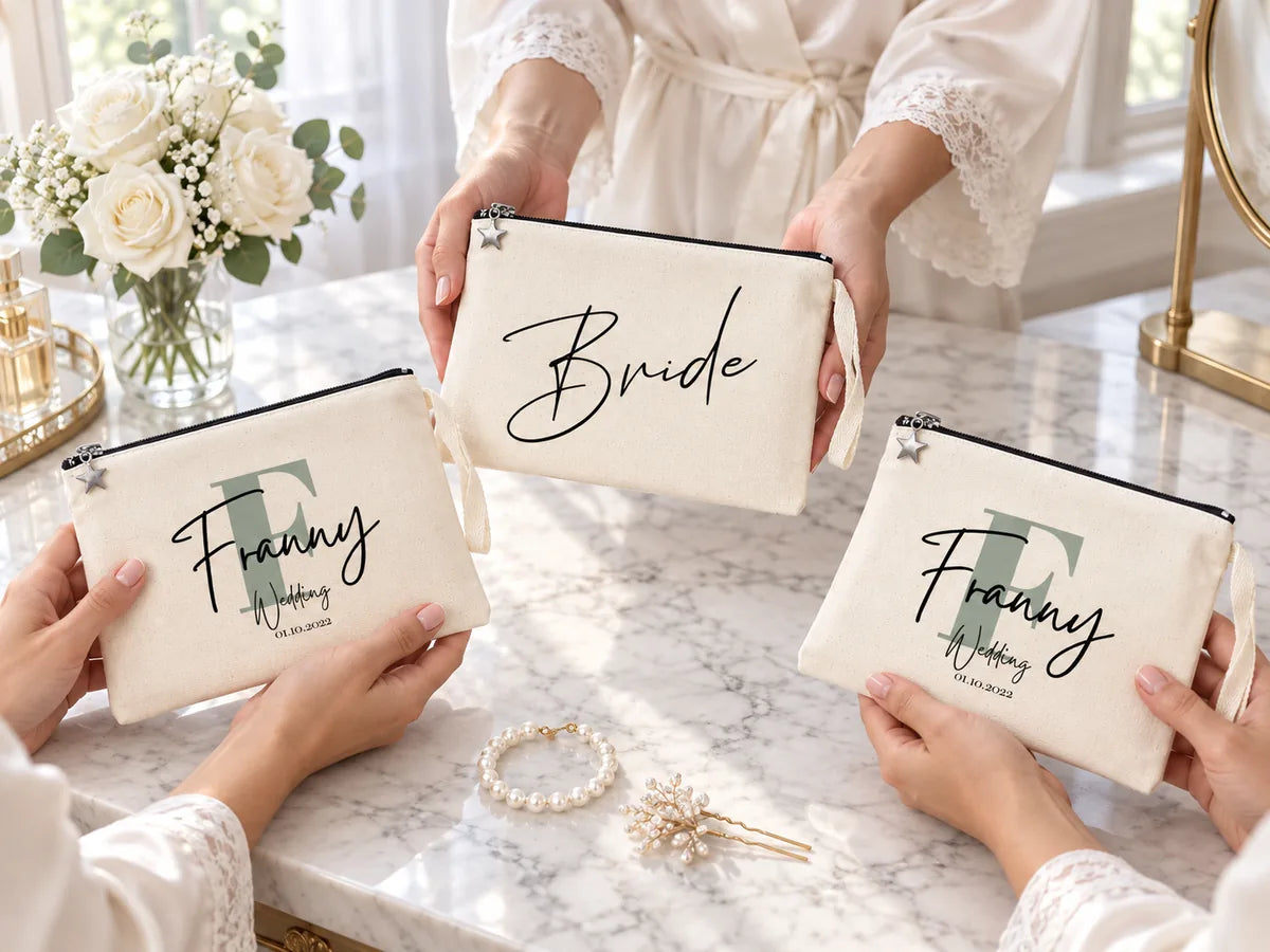 Hände von Brautjungfern in Seidenkimonos an einem Marmor-Schminktisch mit einer „Bride“-Clutch und zwei „Franny Wedding“-Clutches aus Baumwolle, weißen Rosen und einem Perlenarmband